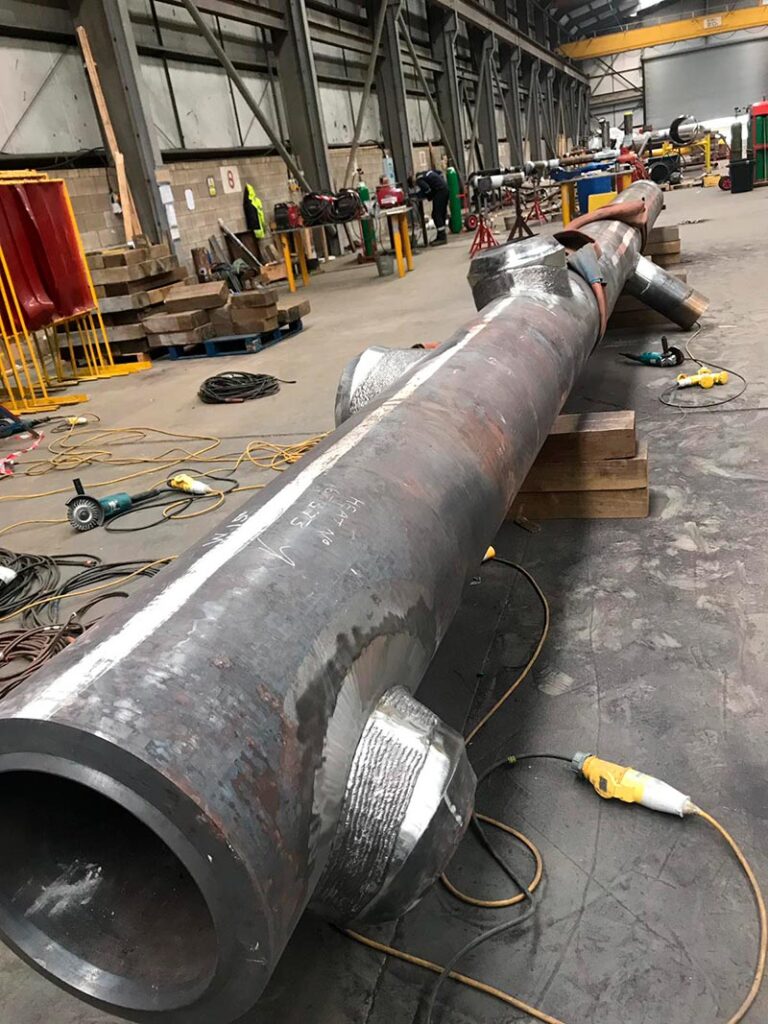 Una imagen de un taller industrial donde se muestra un gran tubo metálico en proceso de fabricación o reparación.